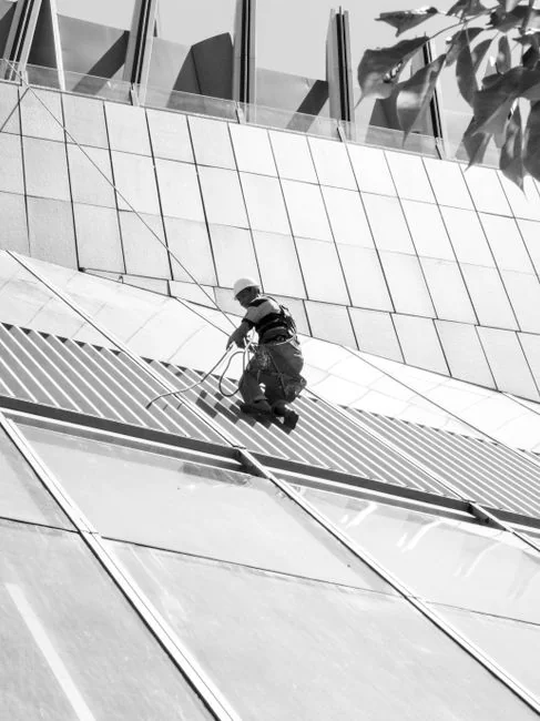 Deux ouvriers nettoient les vitres d’une façade d’immeuble en verre à l’aide d’une plateforme élévatrice, ce qui améliore l’esthétique du bâtiment.